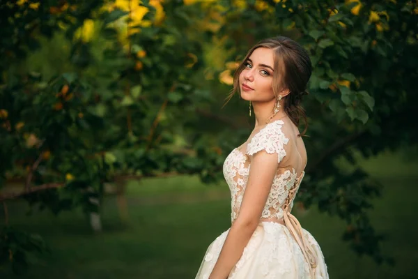 年轻的女孩穿着婚纱时在公园里摆姿势让摄影师。阳光明媚的天气夏天. — 图库照片