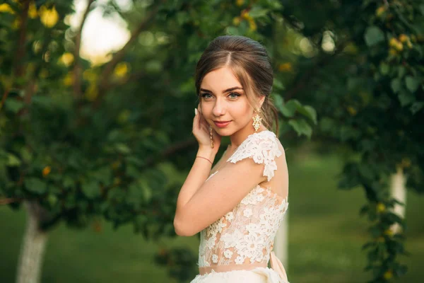 Junges Mädchen im Hochzeitskleid im Park posiert für Fotografen. Sonnenwetter, Sommer. — Stockfoto