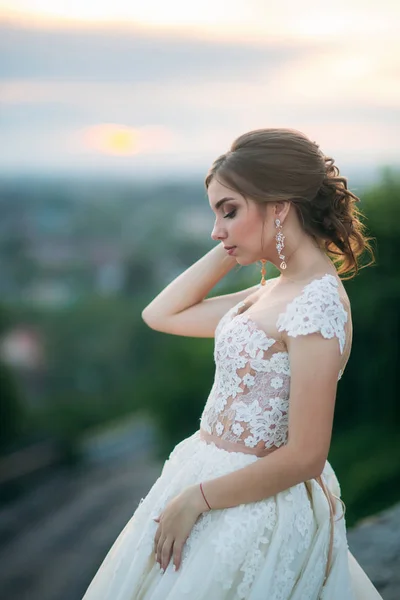 Jong meisje in trouwjurk op de achtergrond van de stad bij zonsondergang. Zomer — Stockfoto