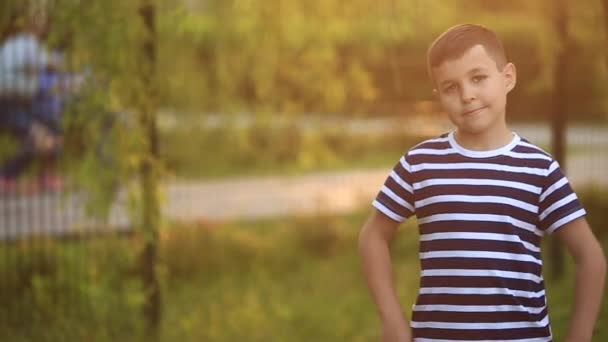 En liten pojke i en randig T-shirt spelar på lekplatsen, gunga på en gunga. Våren. — Stockvideo