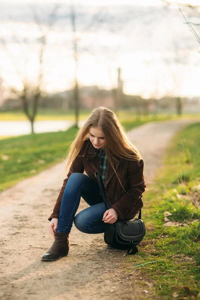 A beautiful girl is walking along the embankment. Blond hair and brown jacket. — Stock Photo, Image