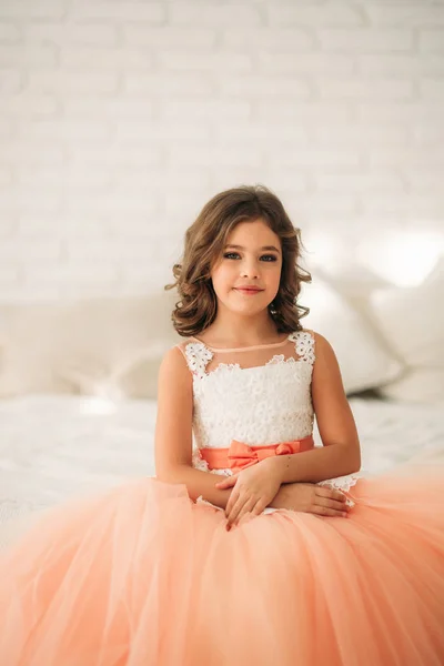 Kleines schönes Mädchen mit braunen Haaren in einem pfirsichfarbenen Kleid. posiert für einen Fotografen — Stockfoto