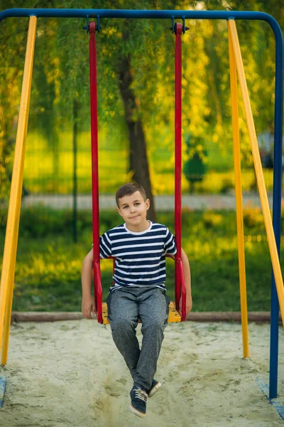 Salıncakta sallanmak, çizgili tişört içinde küçük bir çocuk oyun oynuyor. Çocuk gülümseyen ve tezahürat