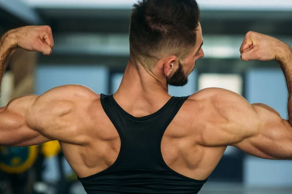 Jovem atleta posando com um tronco para fotografia em um fundo de parede de tijolo. Fisiculturista, atleta com músculos bombeados, resgate de seios e braços. homem — Fotografia de Stock