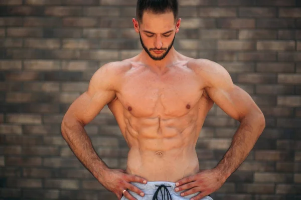 Jeune athlète posant avec un torse pour la photographie sur un fond de mur de briques. Bodybuilder, athlète avec muscles pompés, sauvetage des seins et des bras — Photo