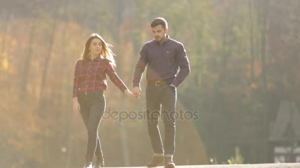 Um casal amoroso caminha no outono no parque. Uma história de amor num dia ensolarado de Outono. lago e franja  . — Vídeo de Stock