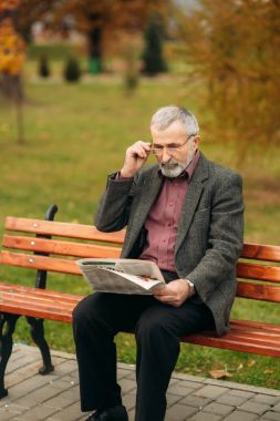 Gri ceketli güzel sakallı güzel Dede parkta bir bankta oturur ve bir gazete okuyor
