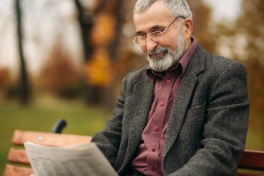 Gri ceketli güzel sakallı güzel Dede parkta bir bankta oturur ve bir gazete okuyor