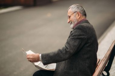 Gri ceketli güzel sakallı güzel Dede parkta bir bankta oturur ve bir gazete okuyor
