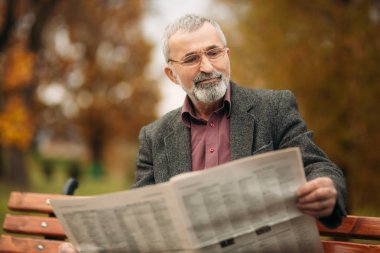 Gri ceketli güzel sakallı güzel Dede parkta bir bankta oturur ve bir gazete okuyor
