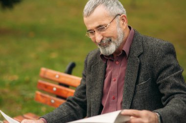 Gri ceketli güzel sakallı güzel Dede parkta bir bankta oturur ve bir gazete okuyor