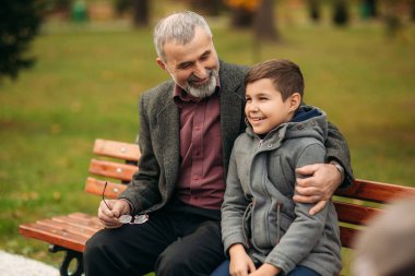 Dede ve torunu parkta birlikte vakit. Onlar bankta oturuyorlar. Parkta yürüyüş ve sevindirici
