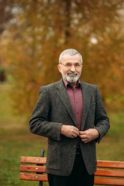 Gözlük takan yakışıklı bir yaşlı adam bir telefon kullanıyor. Sonbaharda Parkta yürümek