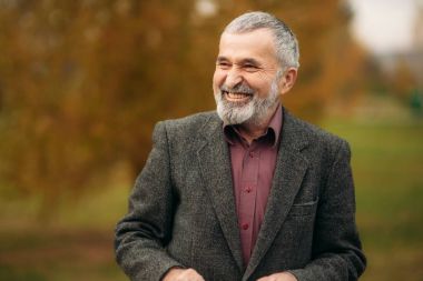 Gözlük takan yakışıklı bir yaşlı adam bir telefon kullanıyor. Sonbaharda Parkta yürümek