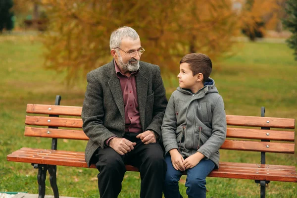 Děda a vnuk spolu strávit čas v parku. Sedí na lavičce. Procházky v parku a radosti — Stock fotografie