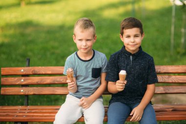 Çocuklar parkta oynuyorlar. İki güzel çocuk T-shirt ve şort gülümseyen eğlenin. Dondurma yemek, sıçrama, çalıştırın. Yaz güneşli