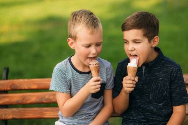 Çocuklar parkta oynuyorlar. İki güzel çocuk T-shirt ve şort gülümseyen eğlenin. Dondurma yemek, sıçrama, çalıştırın. Yaz güneşli