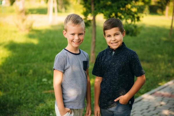 Dos niños juegan en el parque. Dos hermosos chicos en camisetas y pantalones cortos se divierten sonriendo. Comen helado, saltan, corren. El verano es soleado —  Fotos de Stock