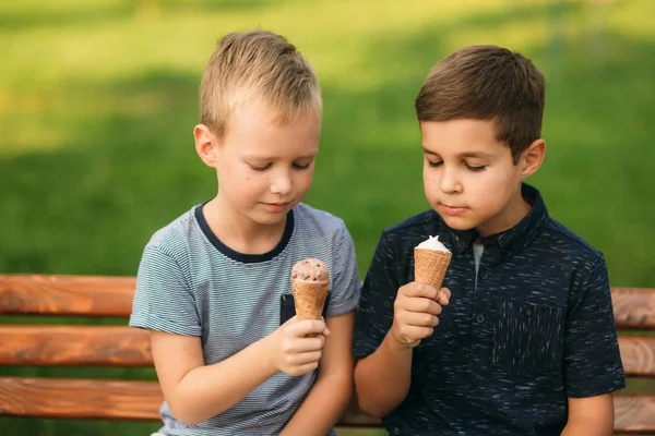 Két gyermek játszik a parkban. Két gyönyörű fiú póló és rövidnadrág szórakozást, mosolyogva. Ők eszik fagylaltot, ugrás, fuss. Nyár sunny — Stock Fotó