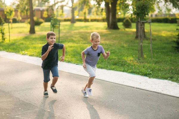 Two children are playing in the park. Two beautiful boys in T-shirts and shorts have fun smiling. They eat ice cream, jump, run. Summer is sunny