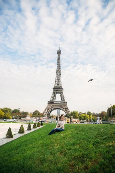 Hermosa chica posando ante el fotógrafo sobre el fondo de la Torre Eiffel. Fotosesión de otoño. Clima soleado. Hermosa sonrisa y maquillaje — Foto de Stock