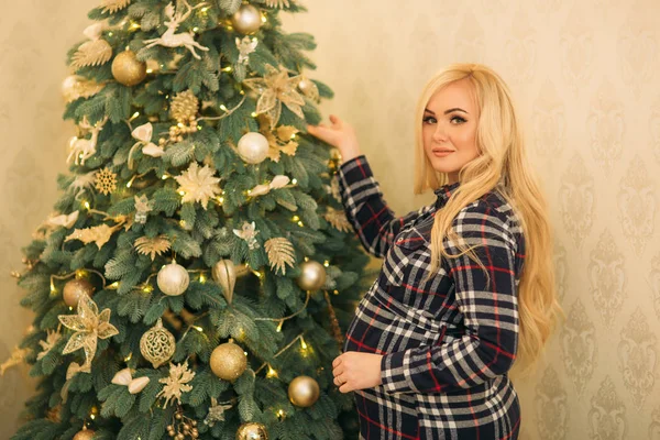 En vacker gravid blond flicka dekorerar en julgran med vackra leksaker. — Stockfoto