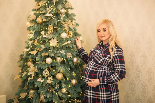 Eine schöne schwangere blonde Mädchen schmückt einen Weihnachtsbaum mit schönen Spielzeugen. — Stockfoto