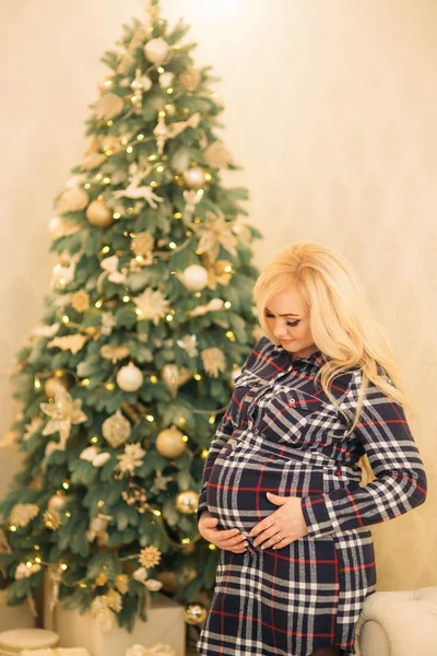 Una hermosa chica rubia embarazada decora un árbol de Navidad con hermosos juguetes . — Foto de Stock