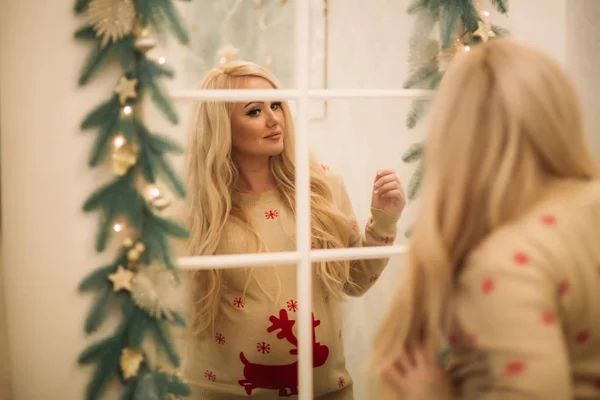En ganska gravid blondin i jul tröja står nära spegeln. — Stockfoto