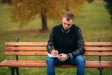 Bir öğrenci bir siyah ceketli bir parkta oturur düşüncelerini bir defter aşağı bir Bank yazıyor. Yakışıklı çocuk