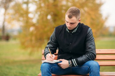 Bir öğrenci bir siyah ceketli bir parkta oturur düşüncelerini bir defter aşağı bir Bank yazıyor. Yakışıklı çocuk