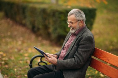 Büyükbaba kullanın pakr bankta oturan bir tablet