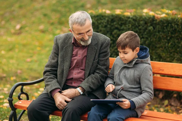 爷爷和他的孙子在公园里一起度过时光。他们坐在长凳上。漫步在公园, 欢庆 — 图库照片