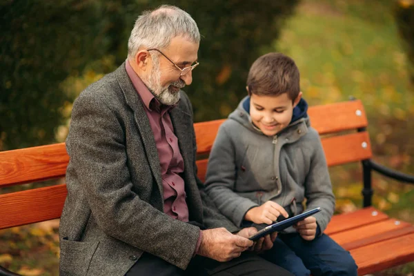 爷爷和他的孙子在公园里一起度过时光。他们坐在长凳上。漫步在公园, 欢庆 — 图库照片