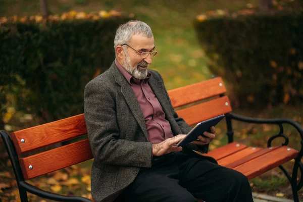 Grand-père utiliser une tablette assis dans le pakr sur le banc — Photo