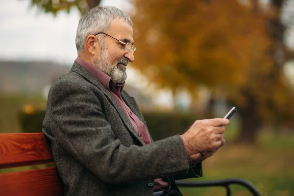 Παππούς χρησιμοποιούν ένα tablet που κάθεται σε του pakr στον πάγκο — Φωτογραφία Αρχείου