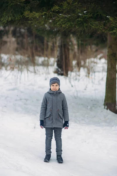 Ein kleiner Junge spaziert bei Winterwetter durch den Park, spielt Schneebälle und freut sich. Warten auf Weihnachtsstimmung — Stockfoto