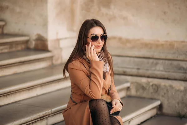 Şık kız kahverengi bir ceket ve gözlüklü bir eşarp. Paris'te bir telefonu kullanarak Fransa. Makyaj — Stok fotoğraf