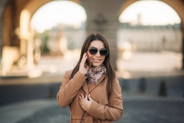 茶色のコートとメガネとスカーフでスタイリッシュな女の子。携帯電話を使用してパリのフランス。化粧 — ストック写真
