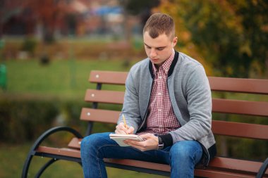 Sevimli öğrenci düşüncelerini defterindeki çiziminden bir kalem kullanarak aşağı yazıyor. Bankta oturur