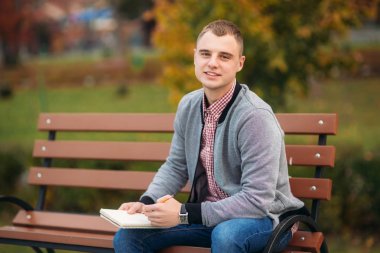 Sevimli öğrenci düşüncelerini defterindeki çiziminden bir kalem kullanarak aşağı yazıyor. Bankta oturur