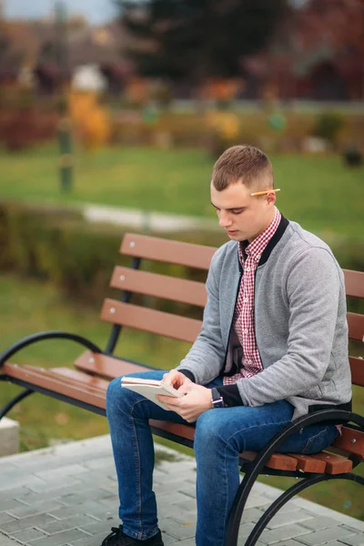 Roztomilá studentka nenapíše své myšlenky do svého zápisníku pomocí tužky. Sedí na lavičce — Stock fotografie