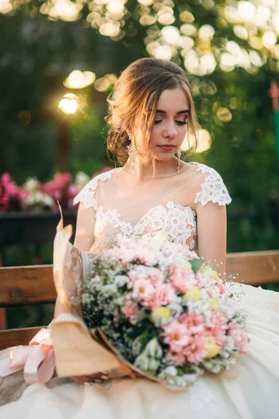 Молодая девушка в свадебном платье в парке позирует для фотографа. Солнечная погода, лето — стоковое фото