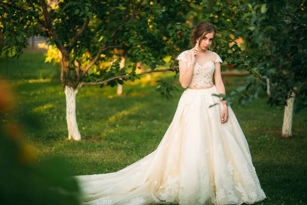 Молодая девушка в свадебном платье в парке позирует для фотографа. Солнечная погода, лето — стоковое фото
