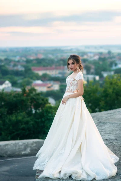 Молодая девушка в свадебном платье на городском фоне на закате. Лето — стоковое фото