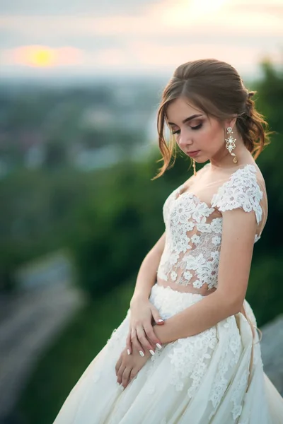 Молода дівчина у весільній сукні на фоні міста на заході сонця. Літо — стокове фото