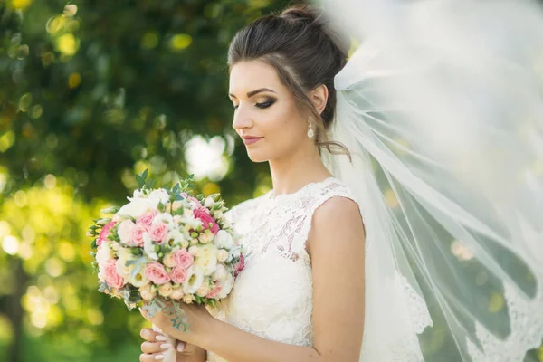 Bella sposa un abito da sposa giocare con un velo nel parco — Foto Stock