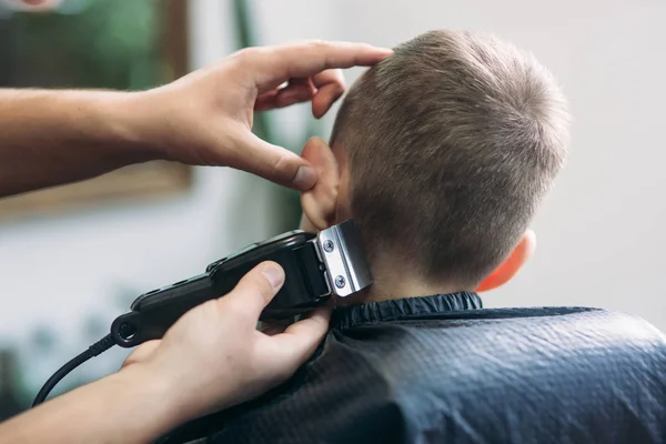 Ammattimainen kampaaja käyttää hiustenleikkuria hiusten hapsuttamiseen pienelle pojalle — kuvapankkivalokuva