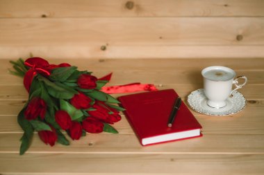Güzel kırmızı lale, lezzetli kapuçino ve ahşap arka plan üzerinde kırmızı not defteri