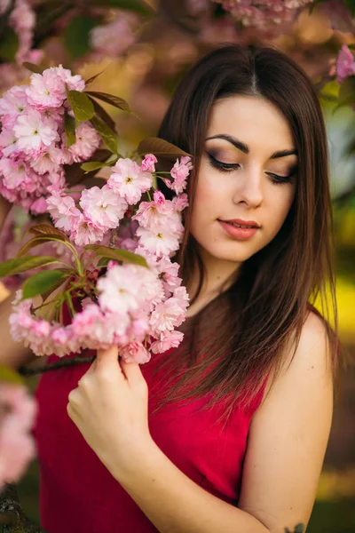 사진을 위해 포즈를 취하는 젊은 여자의 초상화입니다. 백그라운드에서 분홍색 꽃 나무입니다. 봄입니다. 사쿠라 — 스톡 사진